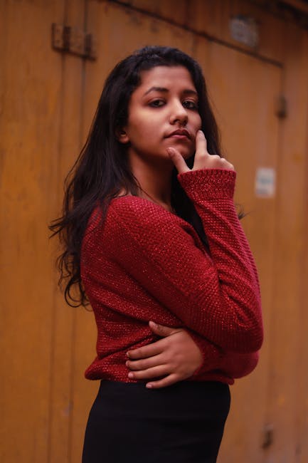 Fashionable woman in a red sweater posing confidently against a wooden backdrop.