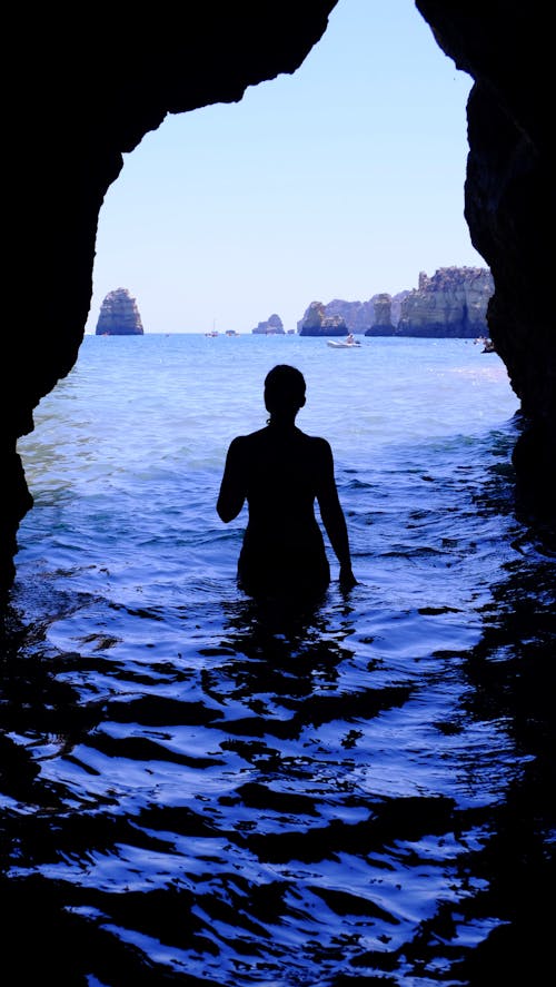 Silhouette of Woman at Blue Sea Inside Black Cave during Daytime