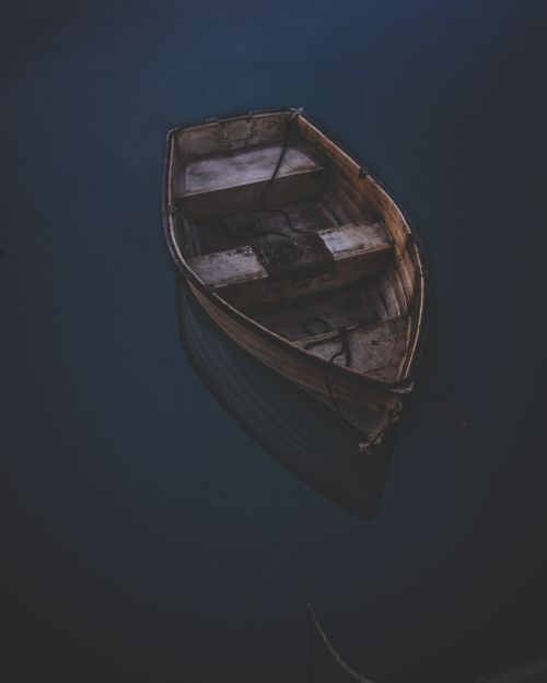 Free An isolated wooden boat gently floats on calm waters during twilight in West Bay, England. Stock Photo