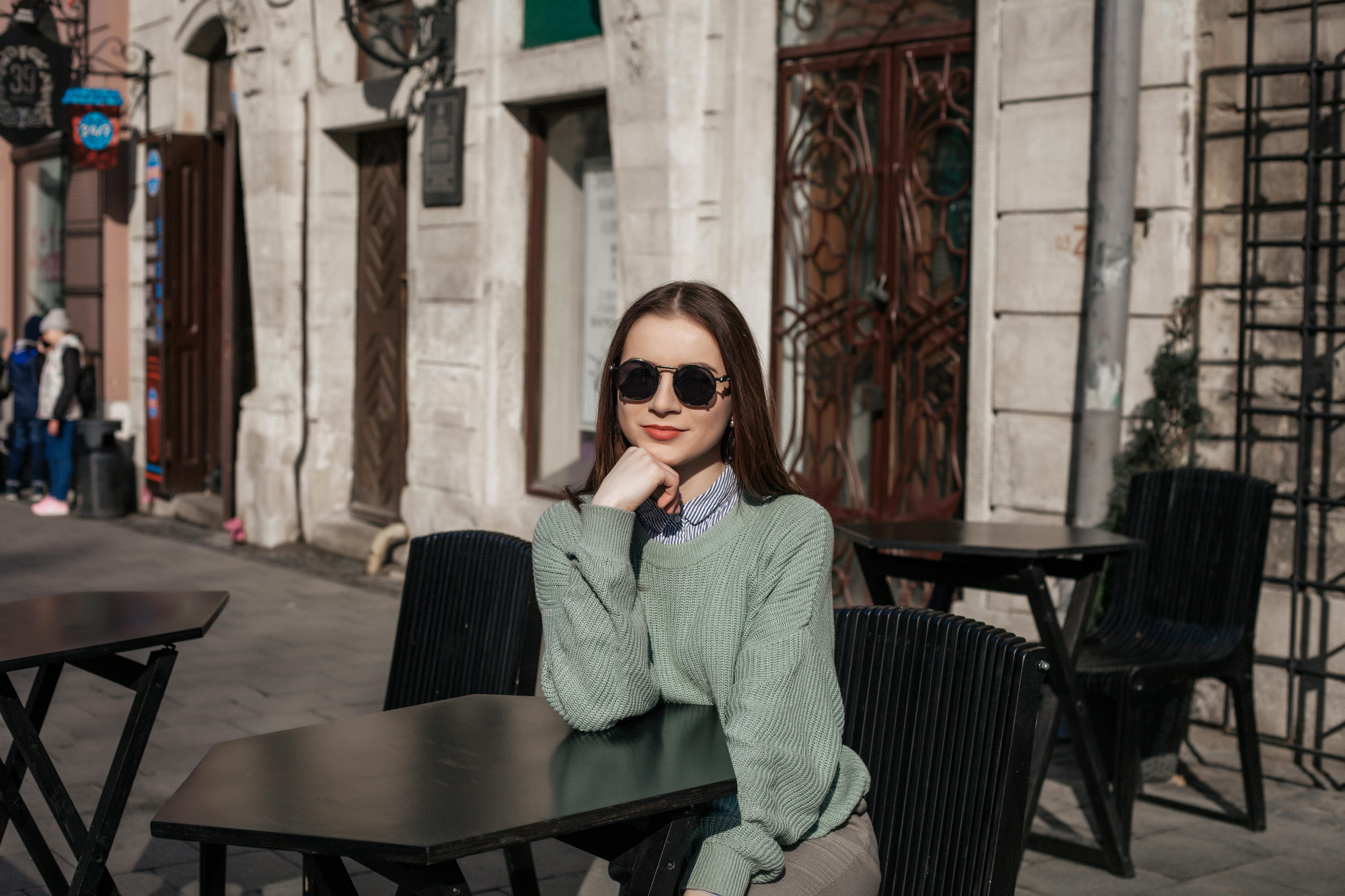 一位时尚女士在城市咖啡馆里，戴着太阳镜享受阳光明媚的日子