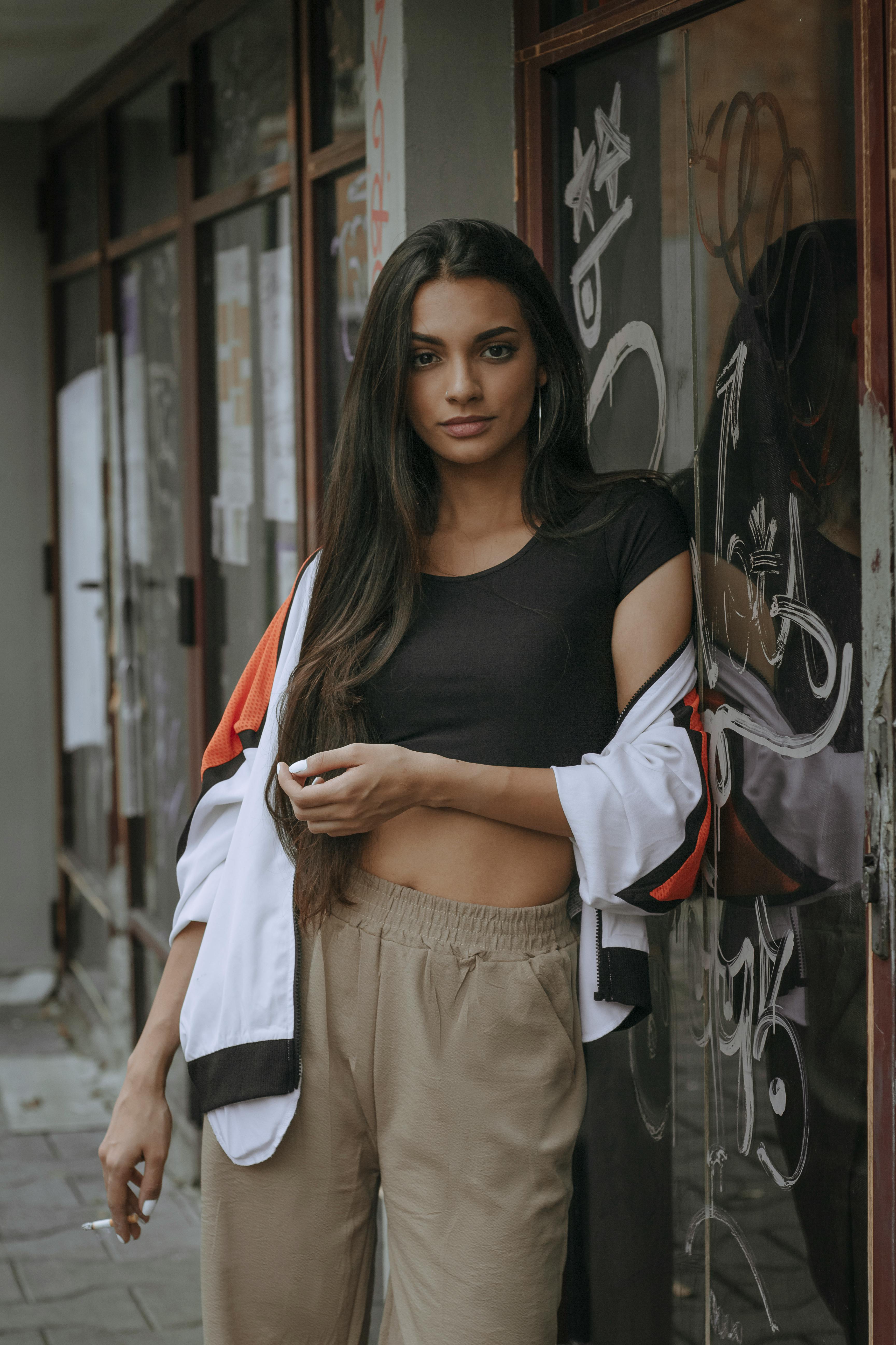 一位长发休闲的年轻女子靠在涂满涂鸦的墙上，手里夹着一支香烟