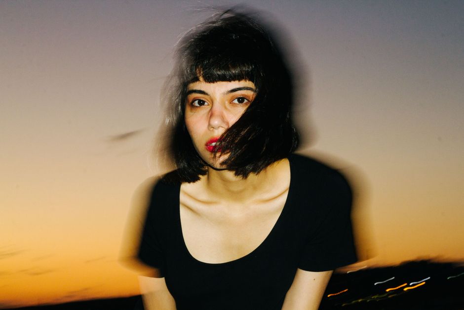 Artistic portrait of a woman with red lips and black hair, blurred against a sunset background.