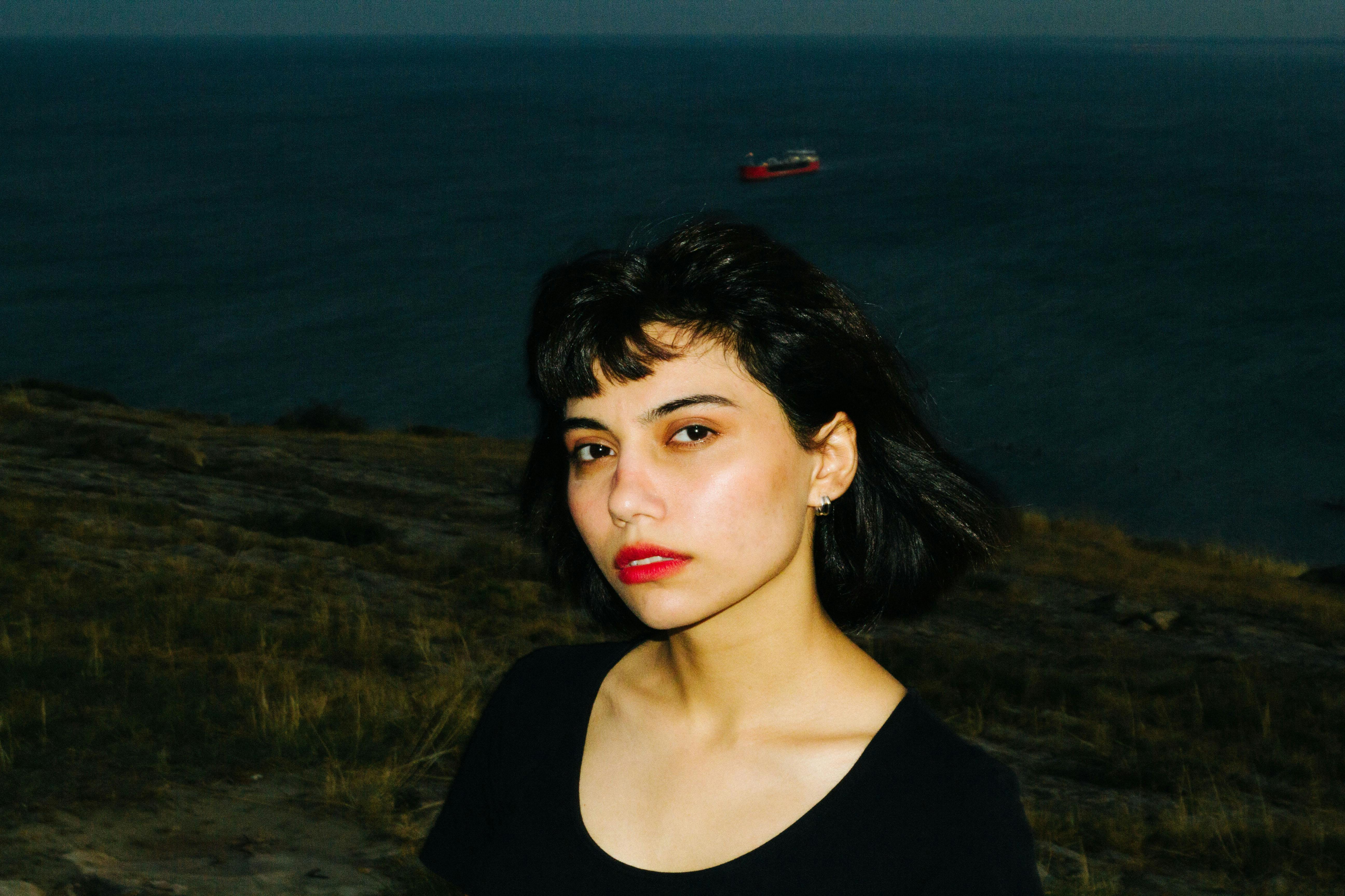 Young woman standing near the sea during dusk, exuding confidence and style.