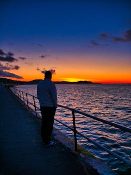 一个人独自站在海滨长廊上，凝视着海上充满活力的日落