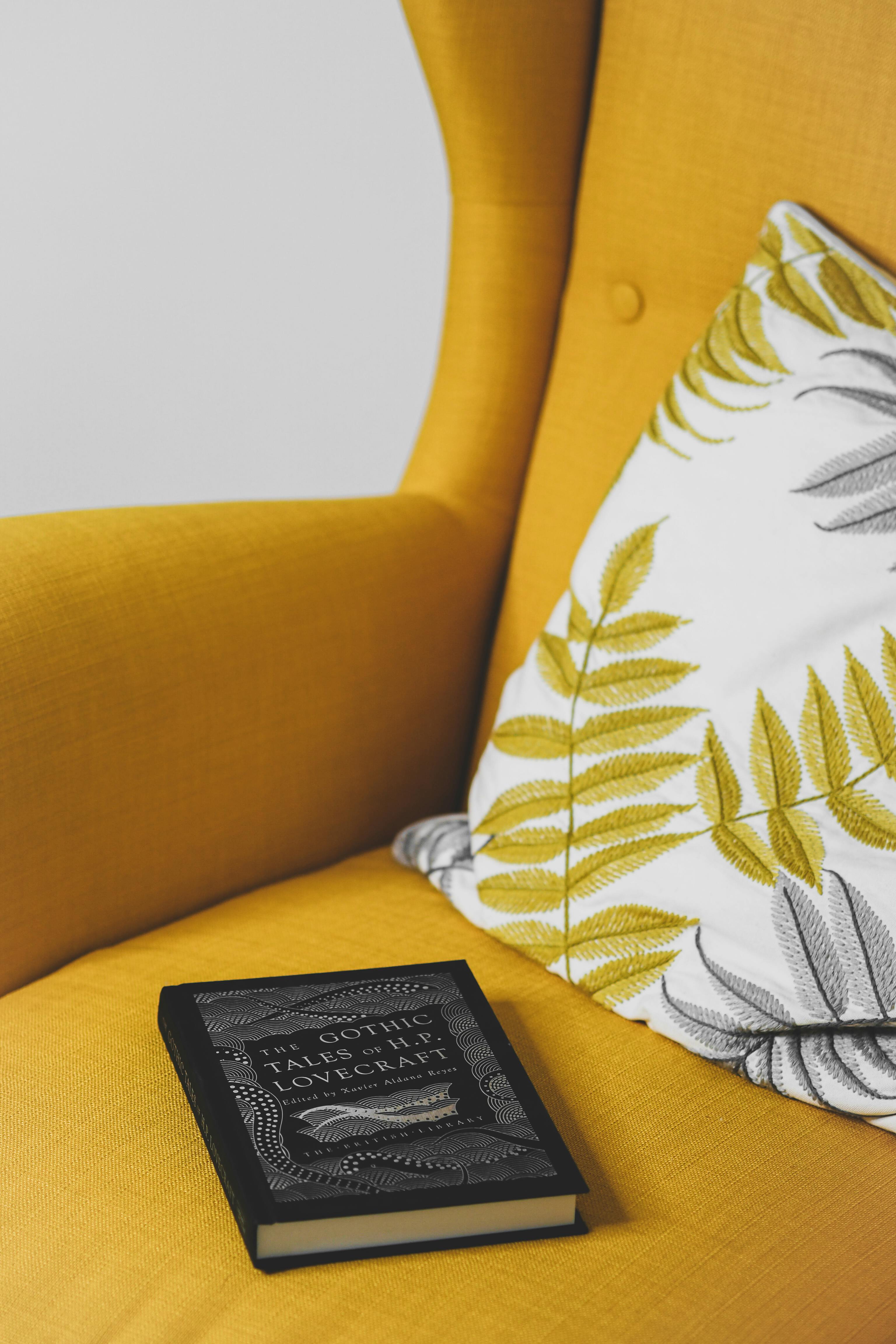 Stylish yellow armchair with a decorative pillow and book, offering a cozy reading nook.