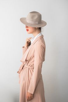Stylish woman wearing a pink coat and fedora hat, side profile in a studio setting.