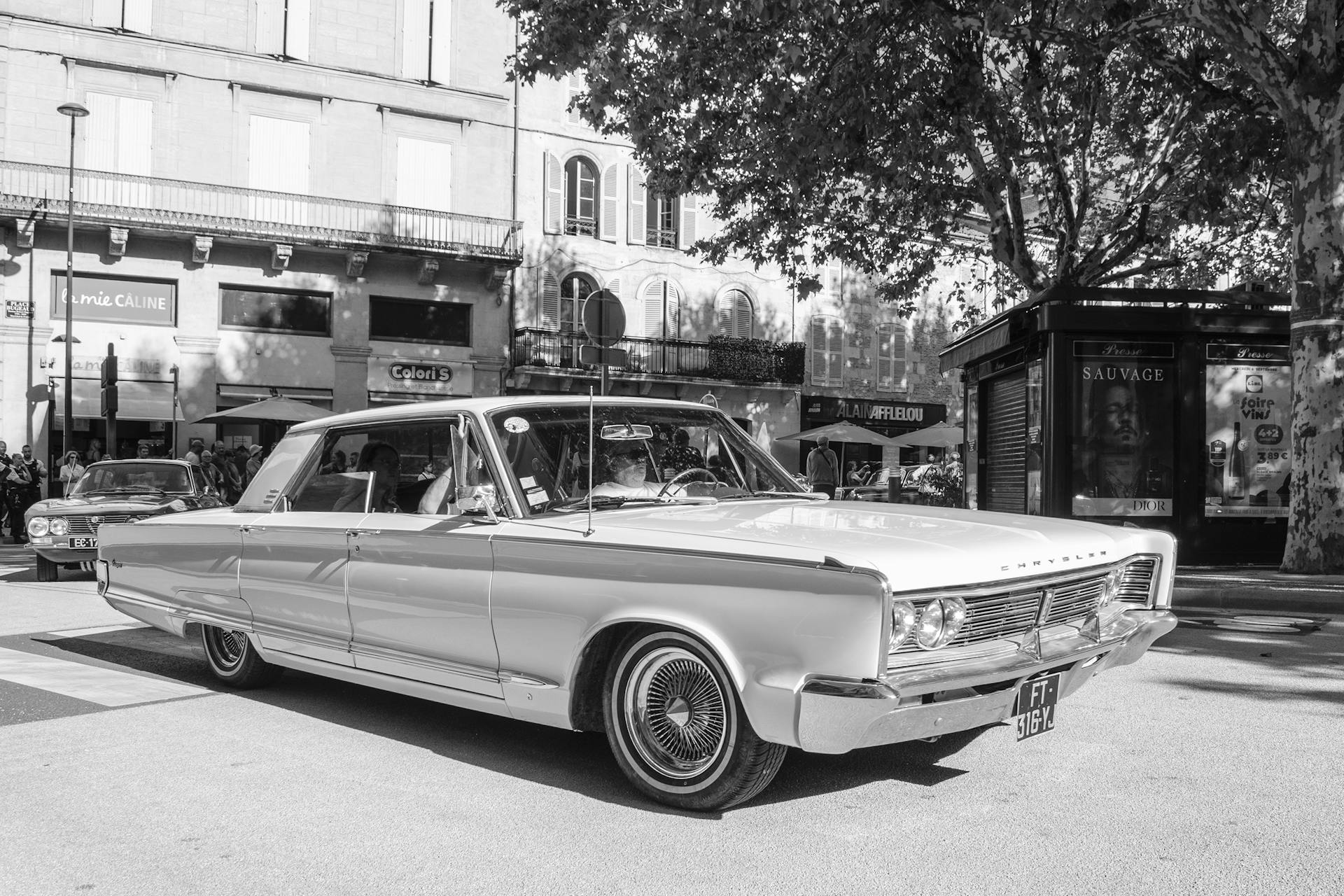 Vintage car driving through Périgueux, France in a black and white cityscape setting.