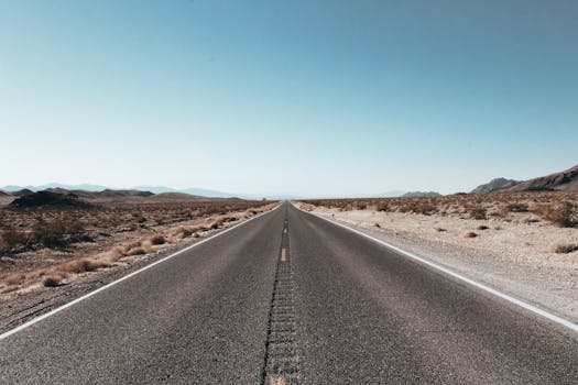 A straight highway stretches through the arid Death Valley desert, under a clear blue sky.