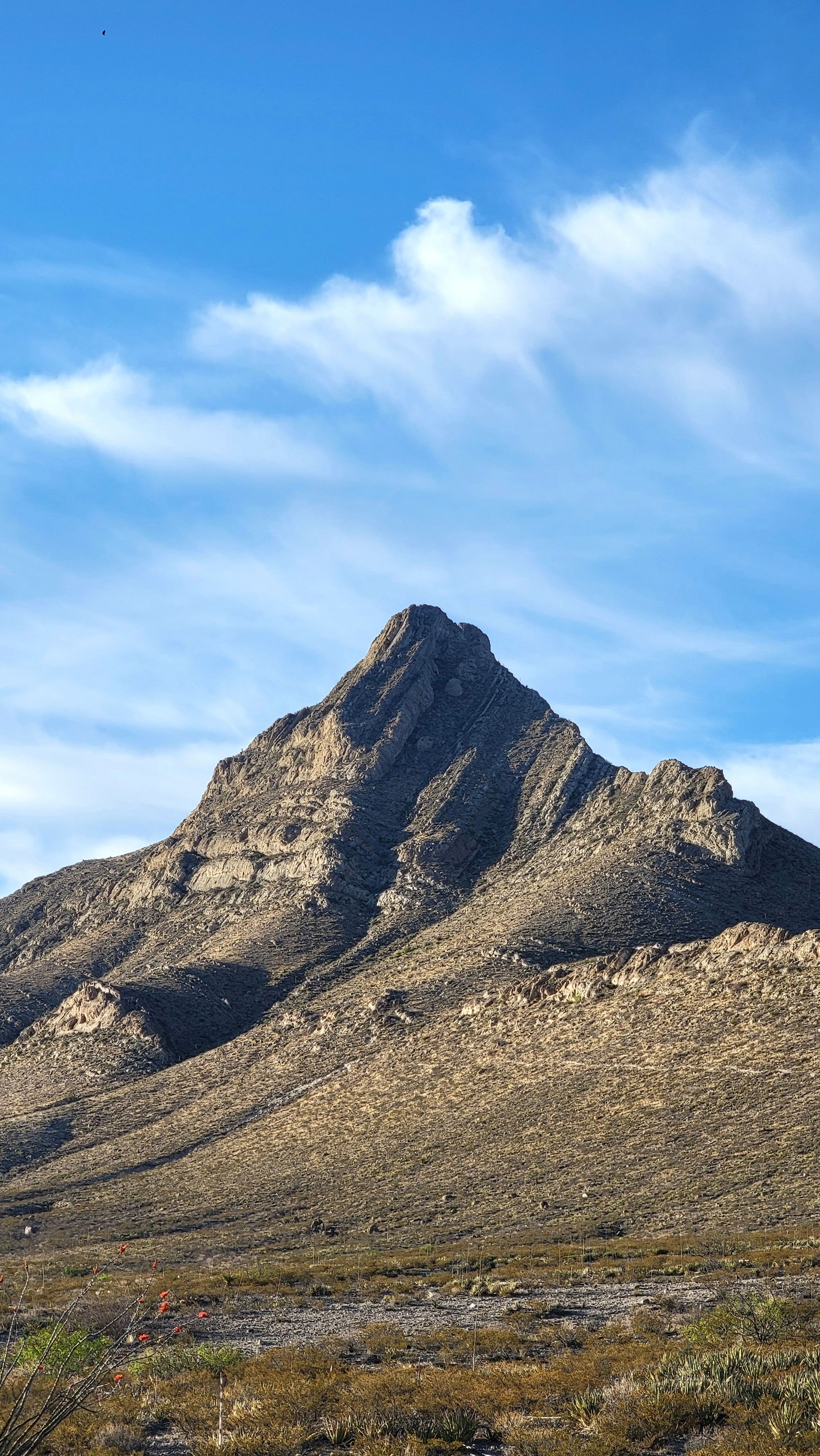 Fotomural Un pico de montaña majestuoso bajo un cielo azul con nubes dispersas, capturando la belleza natural.