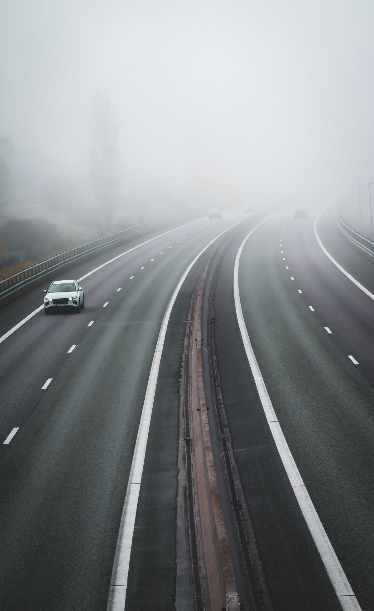 A single car driving on a quiet, foggy motorway in the early morning