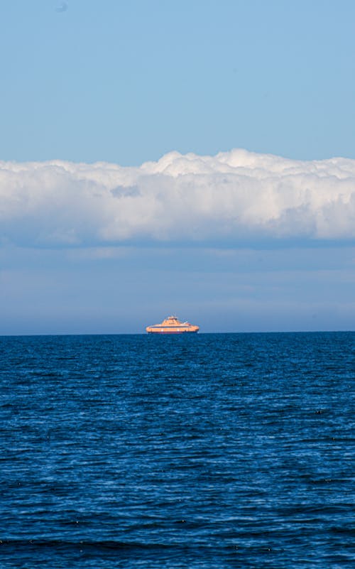 A small boat floating in the ocean with clouds in the sky