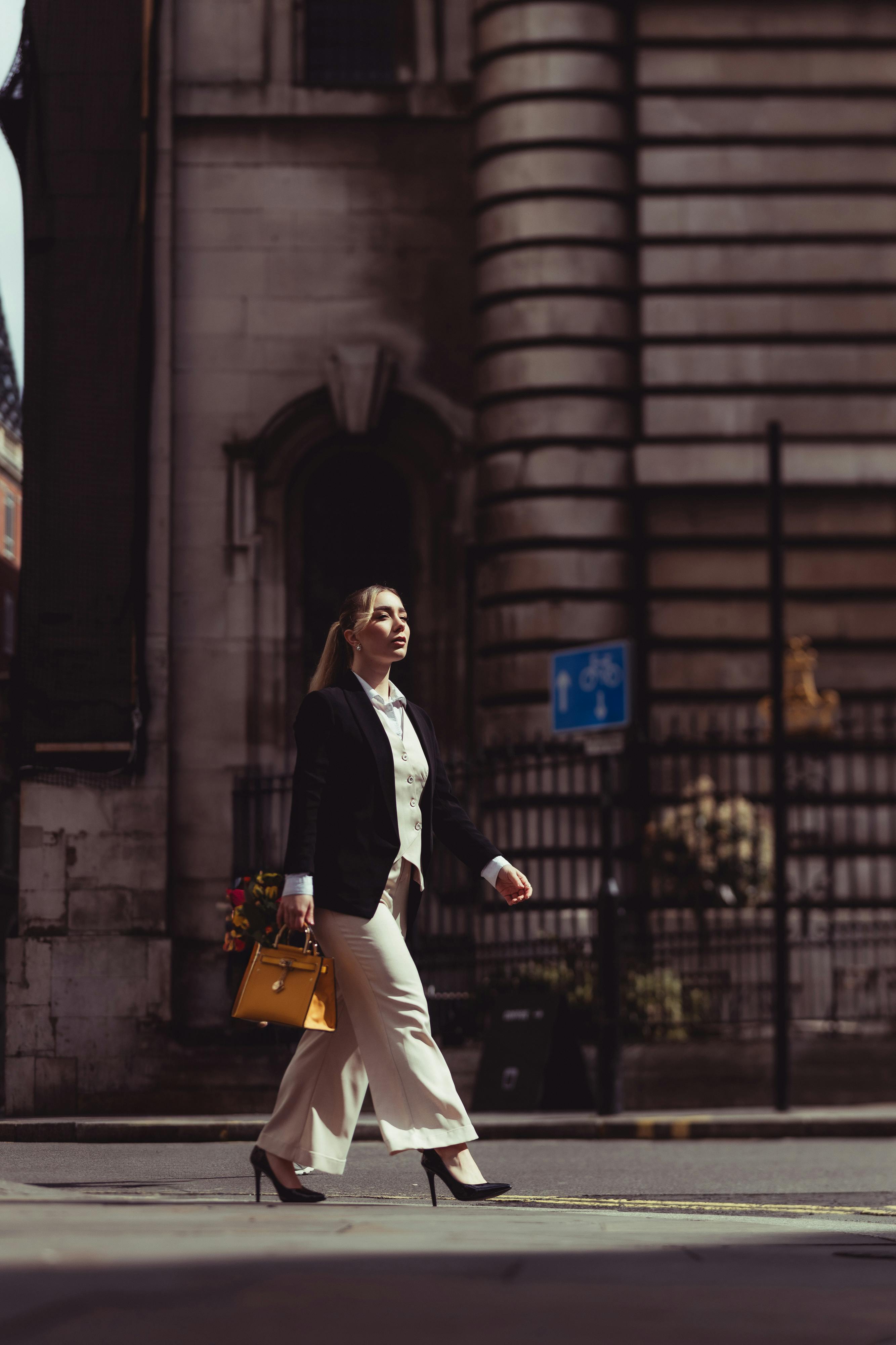 Elegant woman in a suit jacket and high heels walking confidently through city streets.