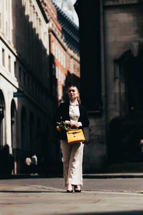 A woman walking down a city street with a yellow bag