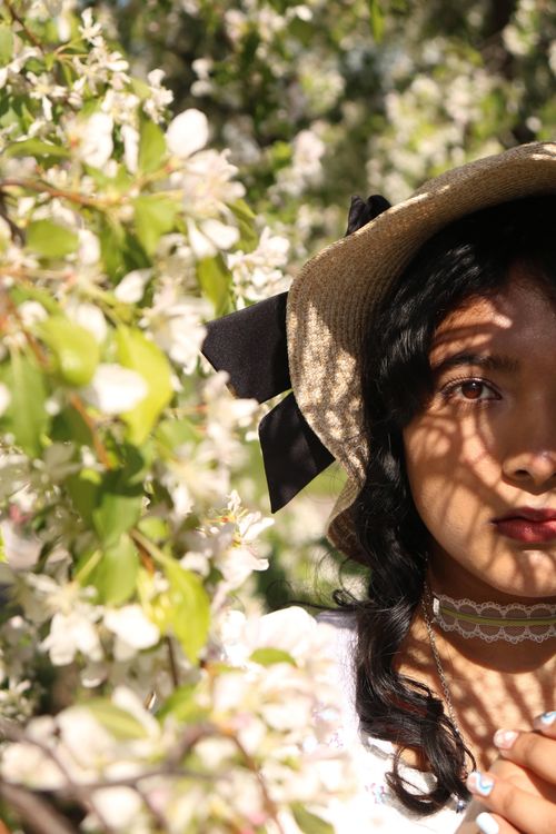 Free A young woman in a sun hat poses amidst blossoming flowers in a sunny garden, showcasing a serene and natural beauty. Stock Photo