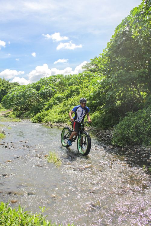 Free Mountain biker riding through a stream in lush Calabarzon landscape, showcasing adventure and nature. Stock Photo