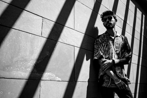 Free Black and white portrait of a fashionable man in sunglasses posing against a wall with dramatic shadows. Stock Photo