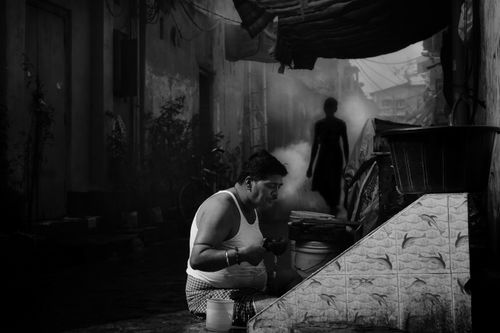 Free A man seated in Kolkata's alley, captured in black and white, evoking urban life. Stock Photo