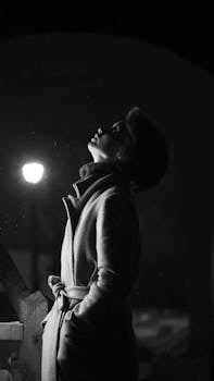 A captivating black and white portrait of a woman in a coat looking up at night.