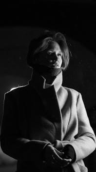 A striking black and white portrait of a person in a coat, set against a night backdrop.