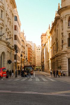 Busy city street in Valencia, Spain, capturing urban life with architecture and pedestrians at sunset.