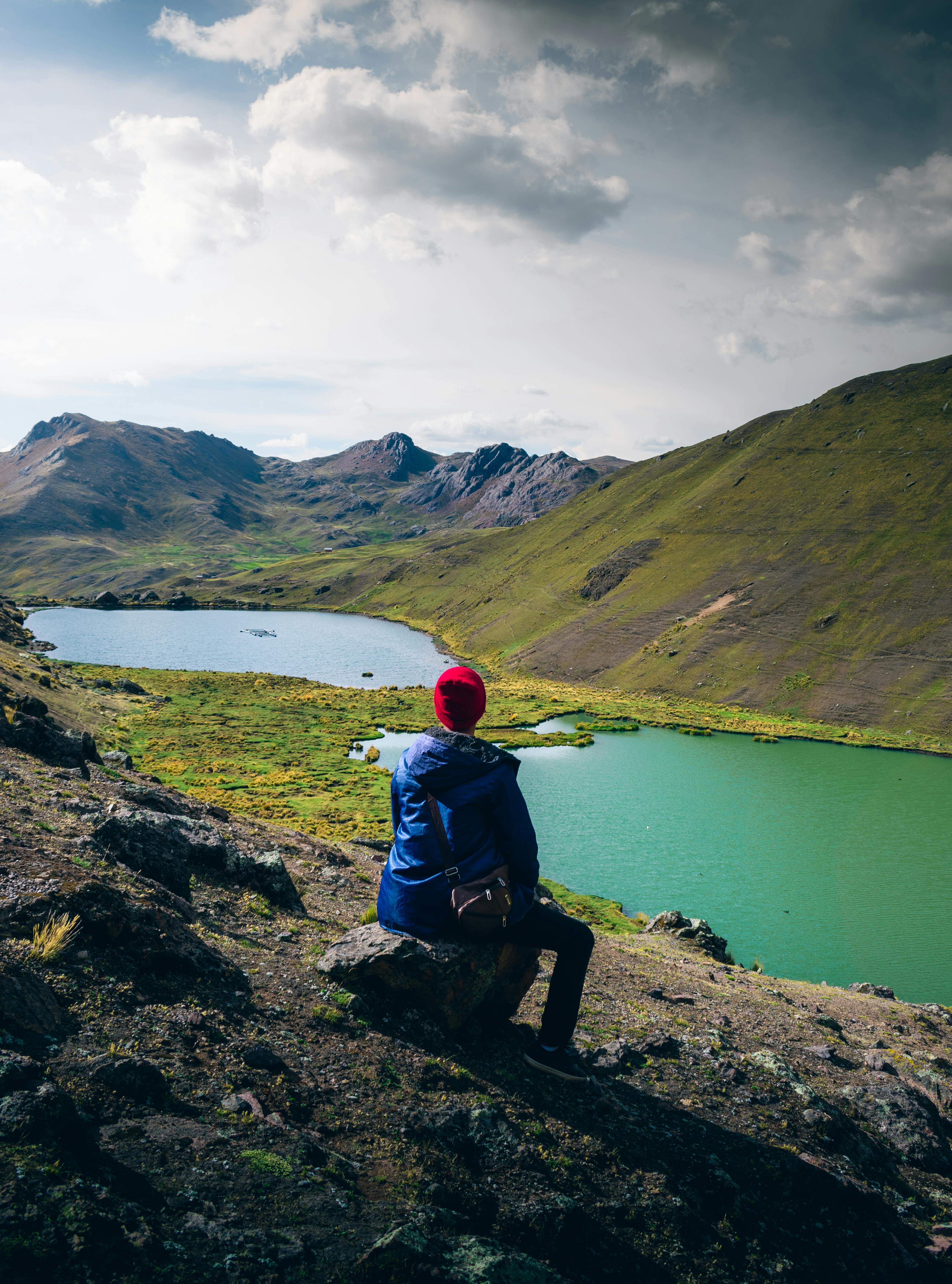 A woman sits overlooking a beautiful mountain lake landscape in Marangani, Cuzco, Peru.