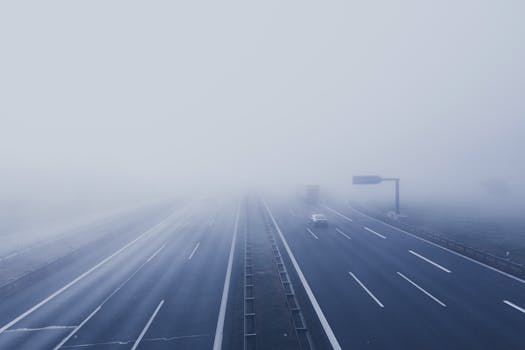 A fog-covered highway with vehicles disappearing into the mist, creating a mysterious and tranquil scene.