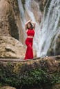 一位年轻女子身着充满活力的红色连衣裙，在瀑布旁优雅地摆着姿势，尽显优雅与自然之美