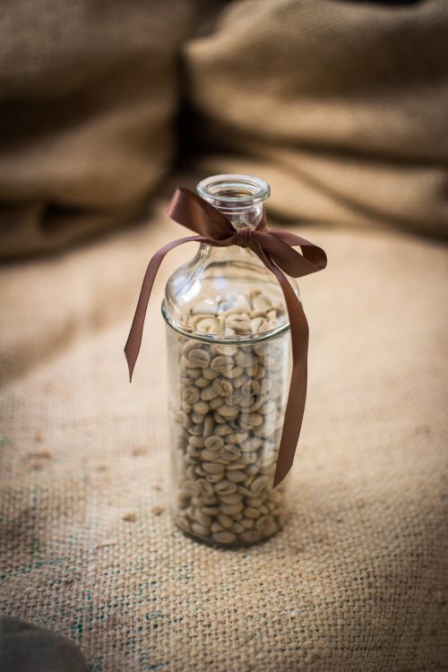 Free Glass bottle filled with unroasted coffee beans, decorated with ribbon on burlap. Stock Photo