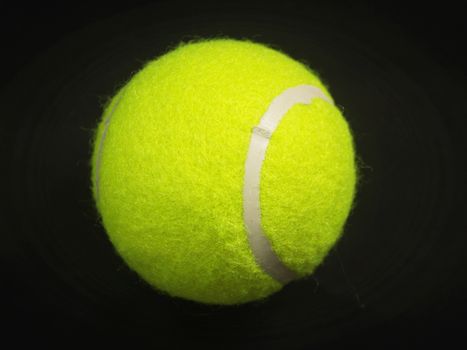 Close-up of a bright yellow tennis ball isolated on a black background.