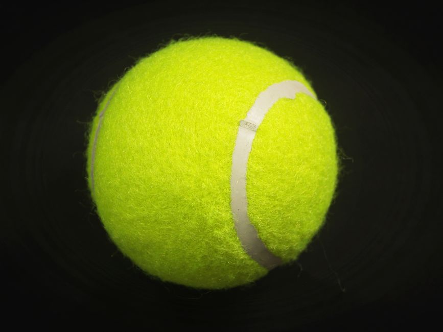 Close-up of a bright yellow tennis ball isolated on a black background.