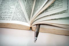 A close-up of an open dictionary with a pen separating the pages for convenient reference.