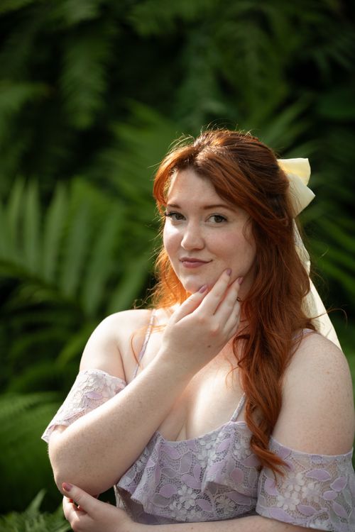 Free Portrait of a red-haired woman in a lace dress amidst vibrant greenery, exuding elegance and charm. Stock Photo