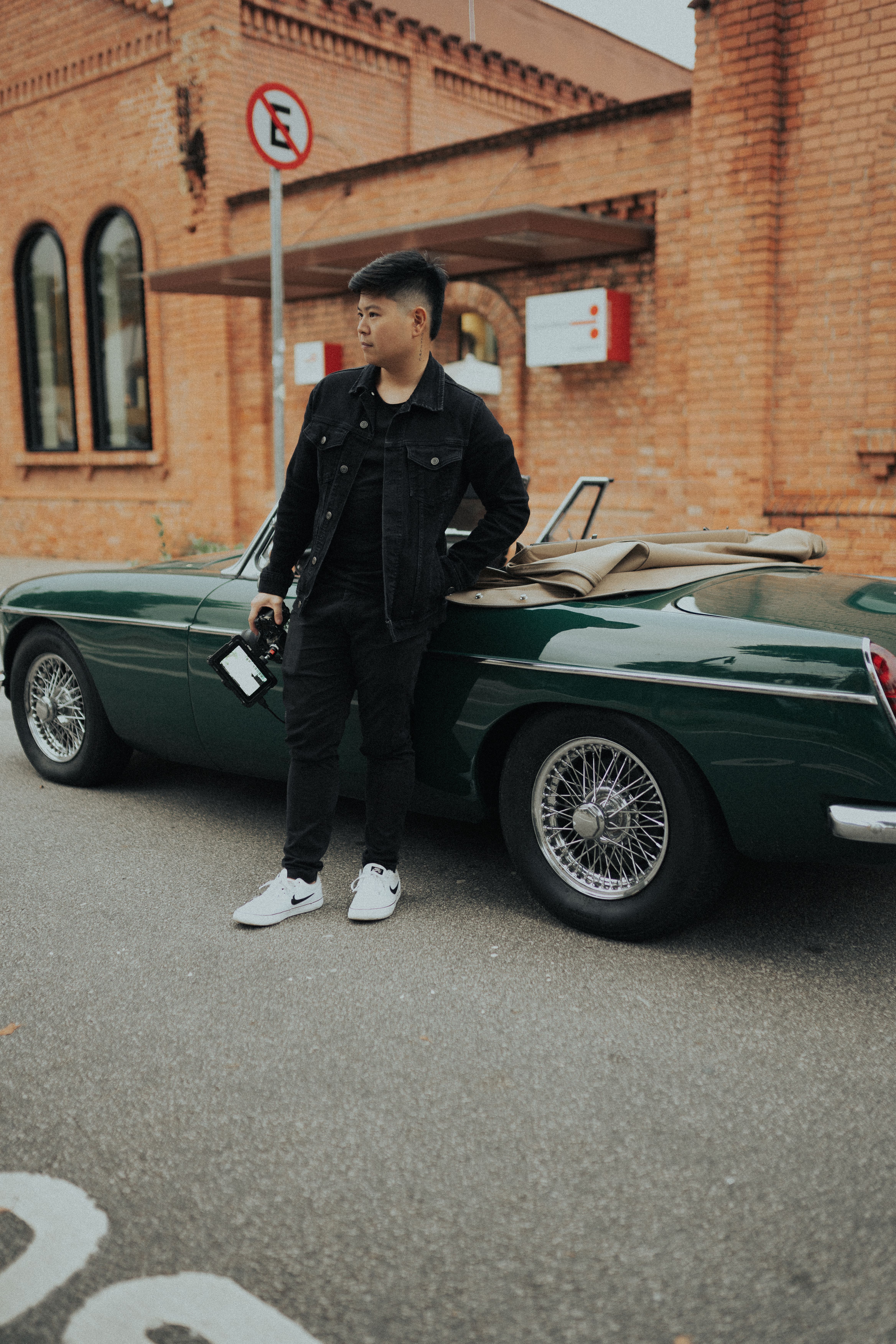 Asian man posing with a vintage convertible car on São Paulo city streets.