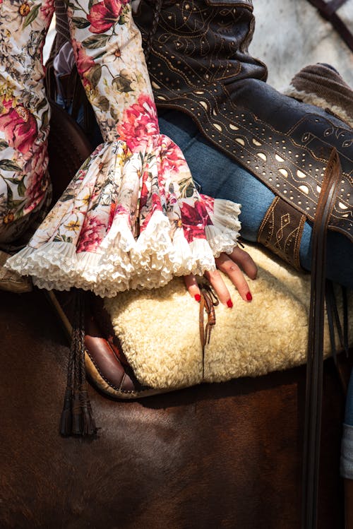 Woman's arm in a ruffled, floral sleeve, resting on a horse saddle