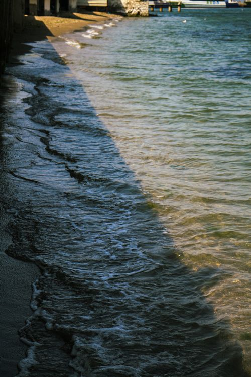 Free Tranquil beach scene with waves and sandy shore under sunlight, offering serene coastal vibes. Stock Photo