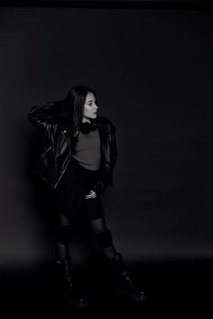 Fashionable woman in black leather jacket with headphones, striking a pose in studio.