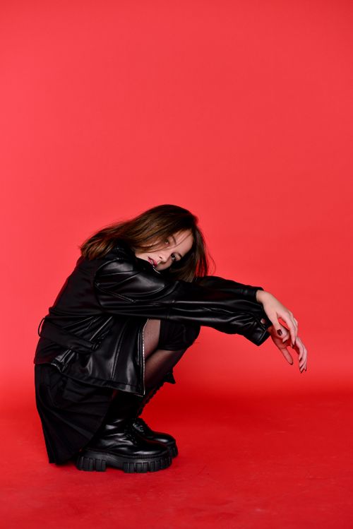 Free Stylish woman squatting in a black leather jacket against a bold red background. Stock Photo