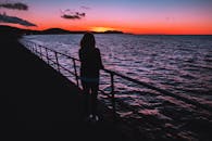 一个女人站在海边，望着宁静的日落，眼前是充满活力的色彩