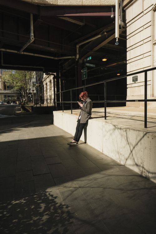 Free A stylish individual leans against a concrete wall in a city street during daylight. Stock Photo