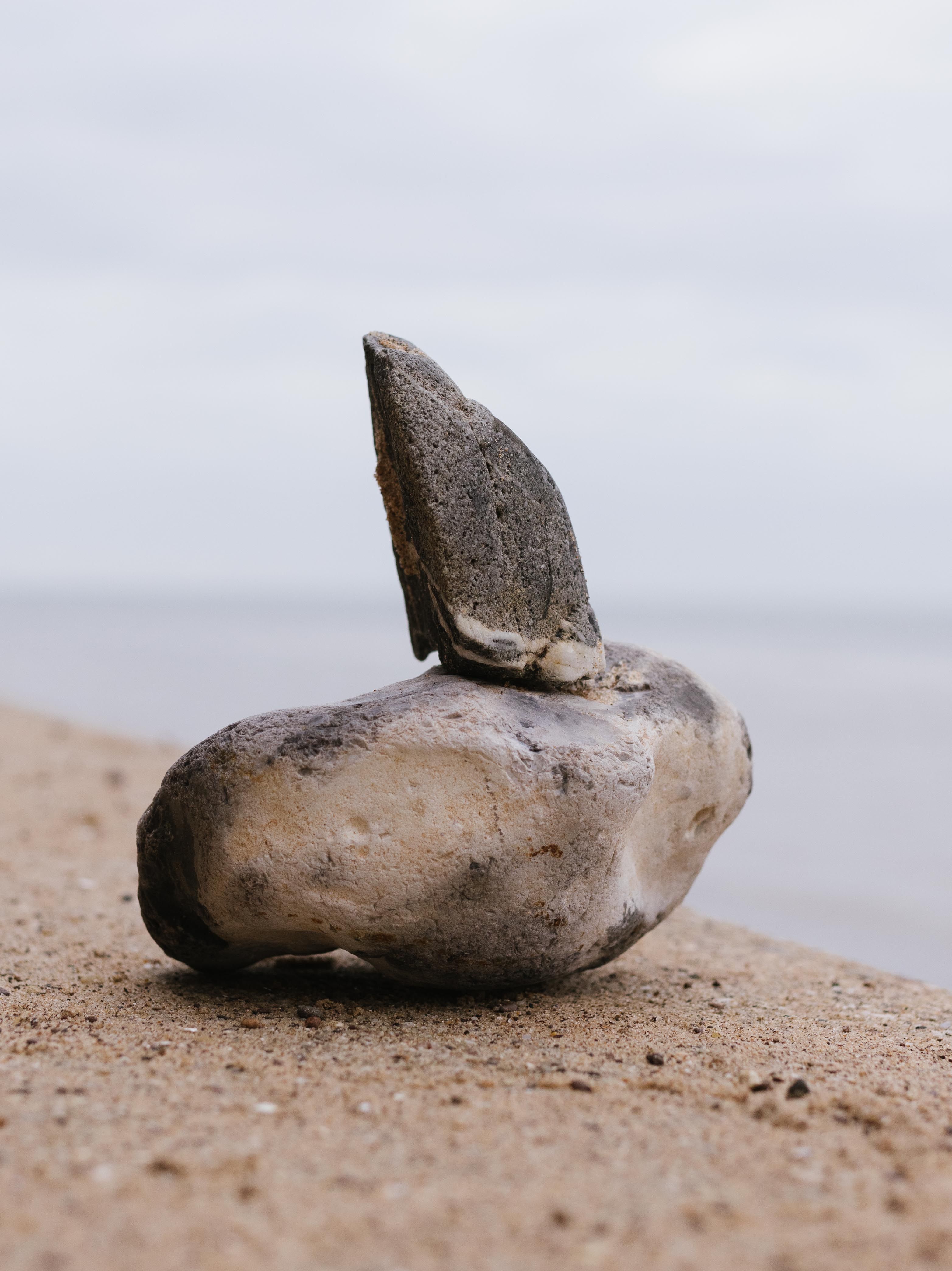 Close-up image of a balanced stone on a sandy beach with the sea in the background.