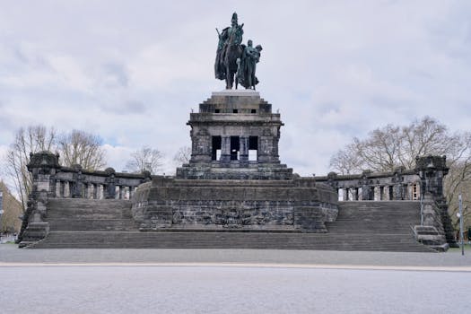 Stunning stone monument in an open park surrounded by bare trees under a cloudy sky.