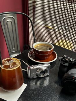 A cozy setup with coffee, iced tea, and cameras on a table near a window.