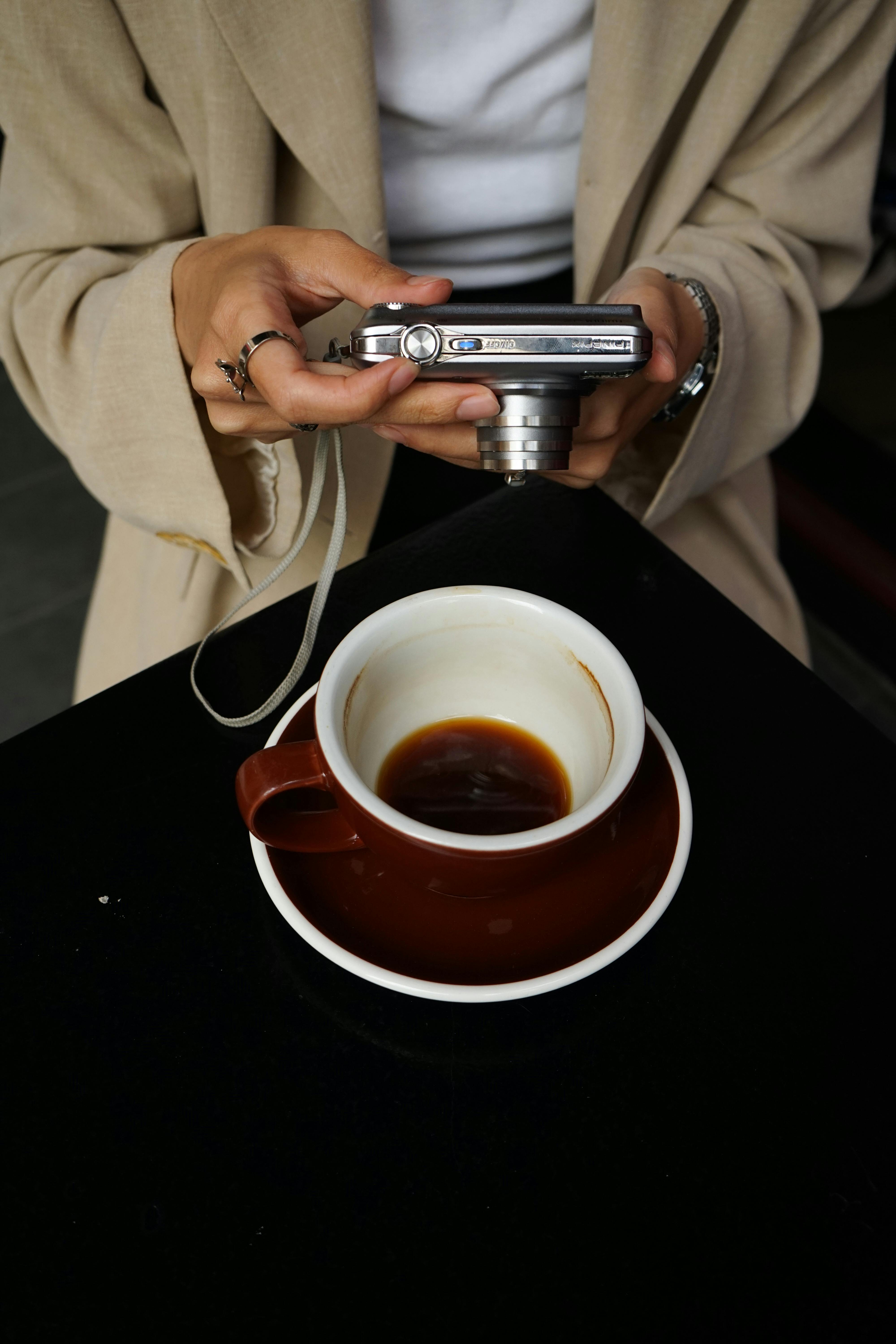A woman holds a camera above a coffee cup, capturing the moment.