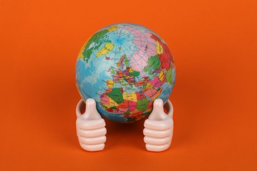 Vibrant globe model with thumbs-up figurines on orange background, symbolizing global positivity. 22669715