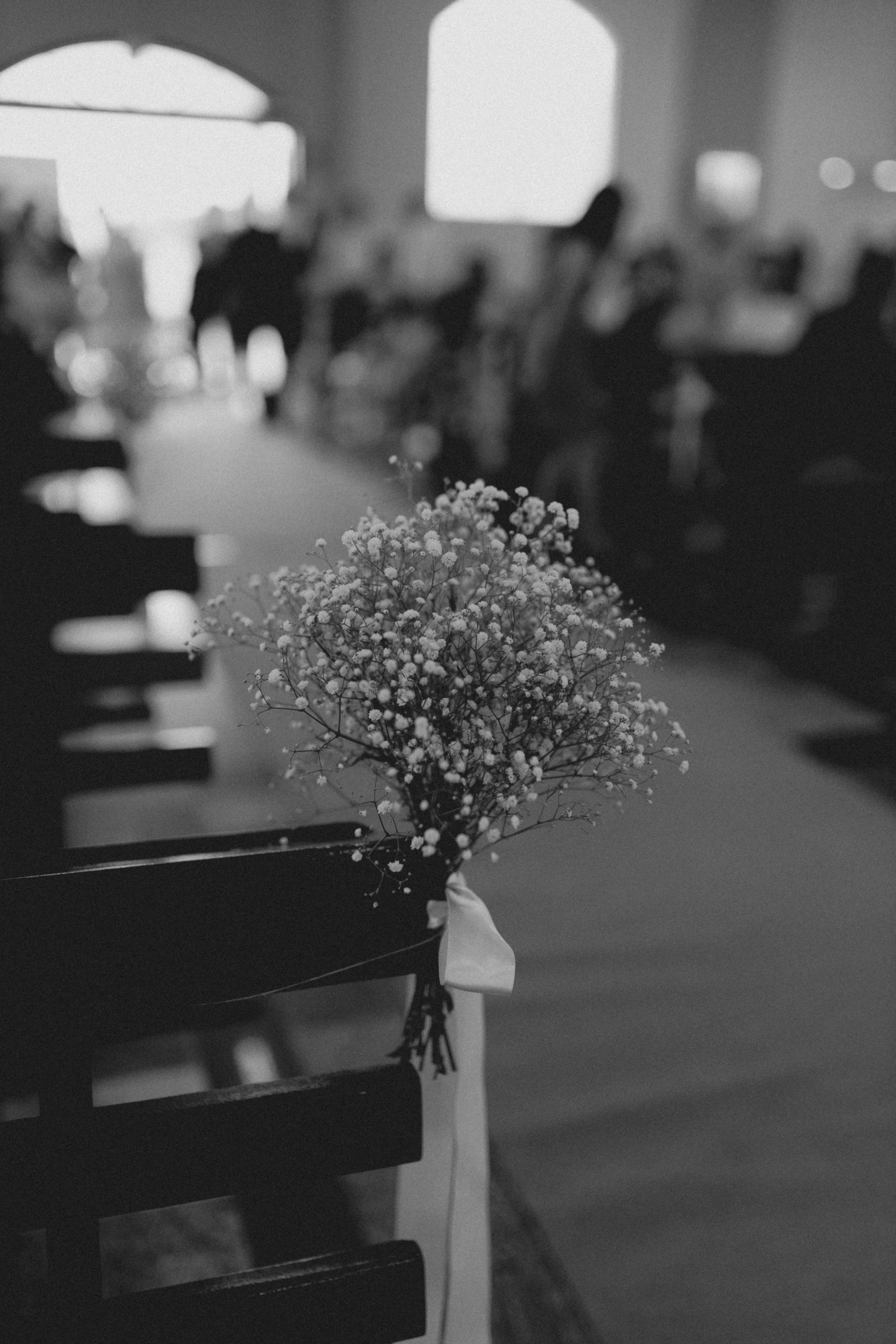 Artistic black and white image capturing a bouquet and aisle seats at a wedding ceremony.