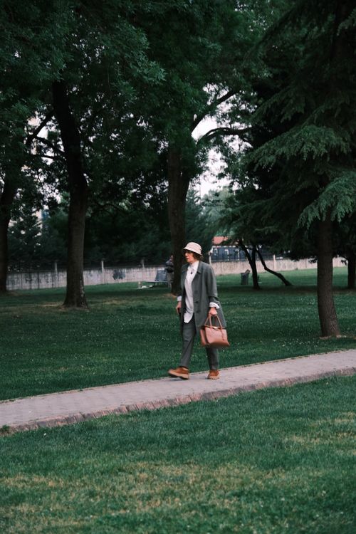 Free Elegant woman walking through a park with a bag, showcasing fashion and nature. Stock Photo