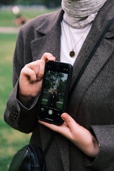 Woman in suit jacket holding smartphone showcasing reflection outdoors.