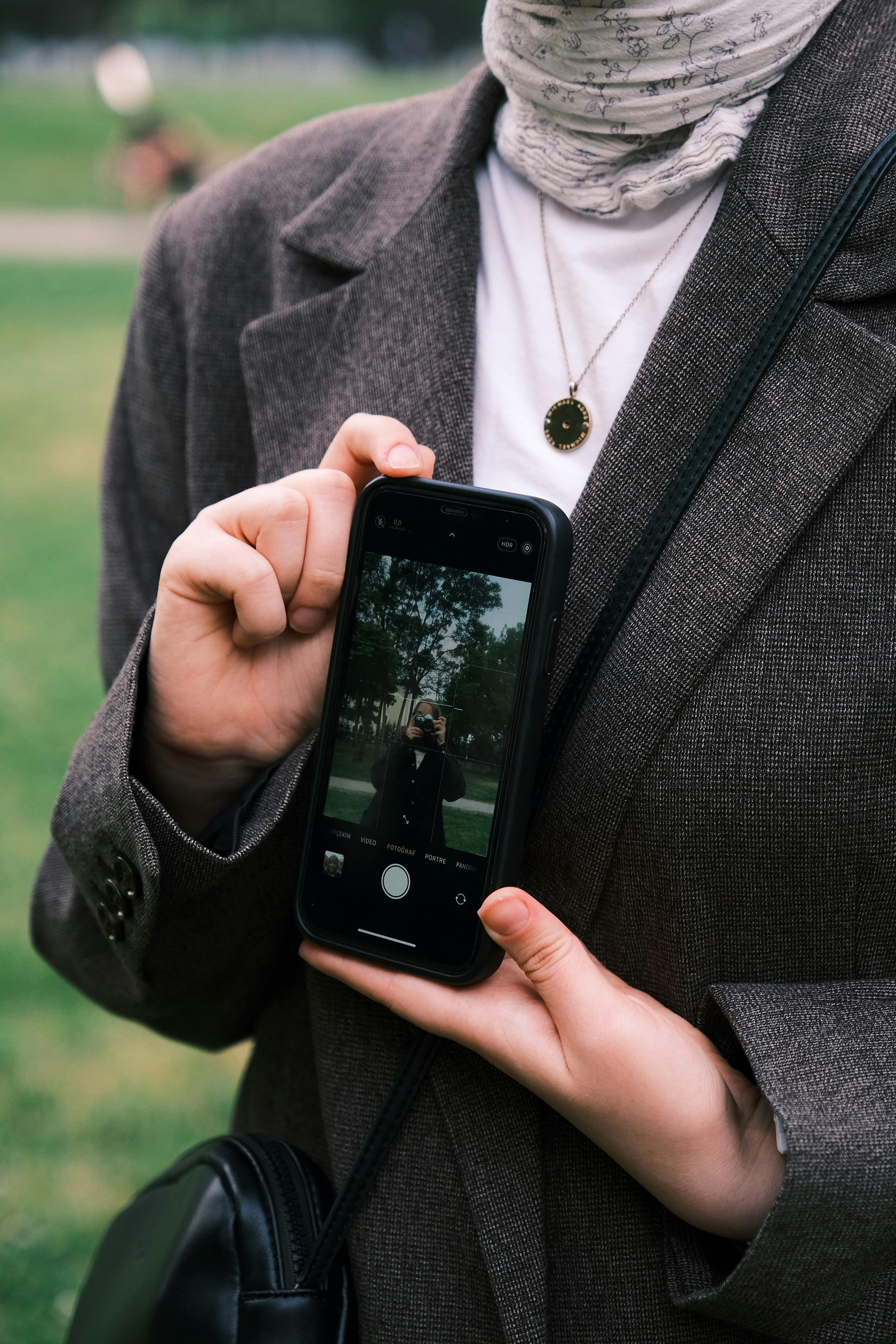 Free Woman in suit jacket holding smartphone showcasing reflection outdoors. Stock Photo