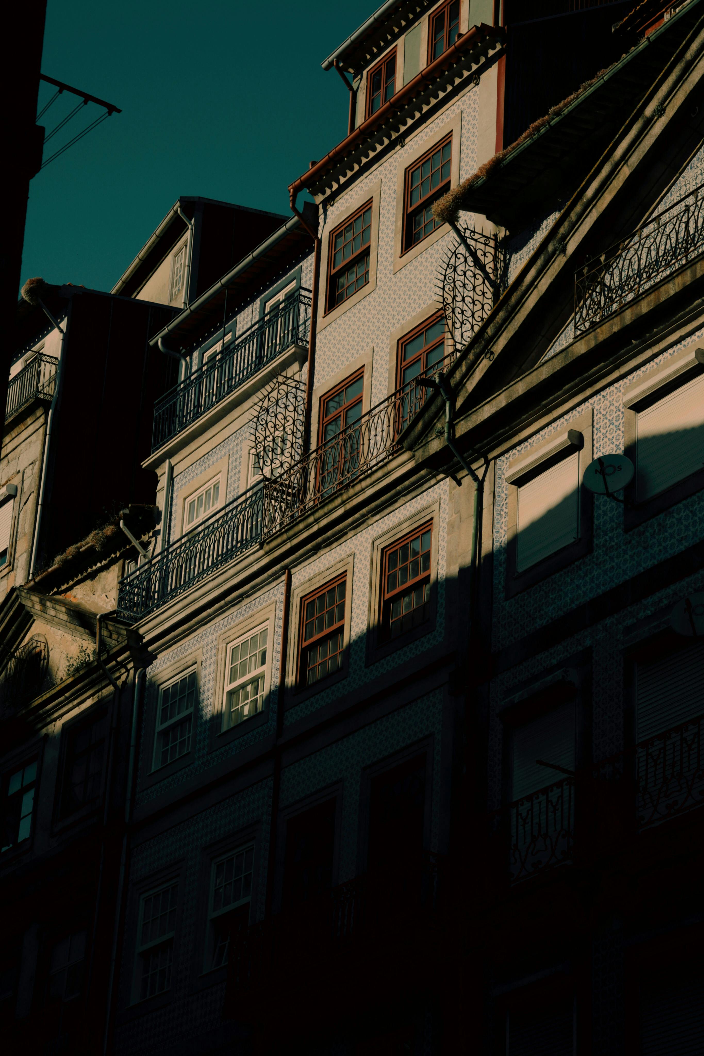 Urban residential buildings in Porto, Portugal, cast in shadow with sunlit highlights, showcasing architectural details.