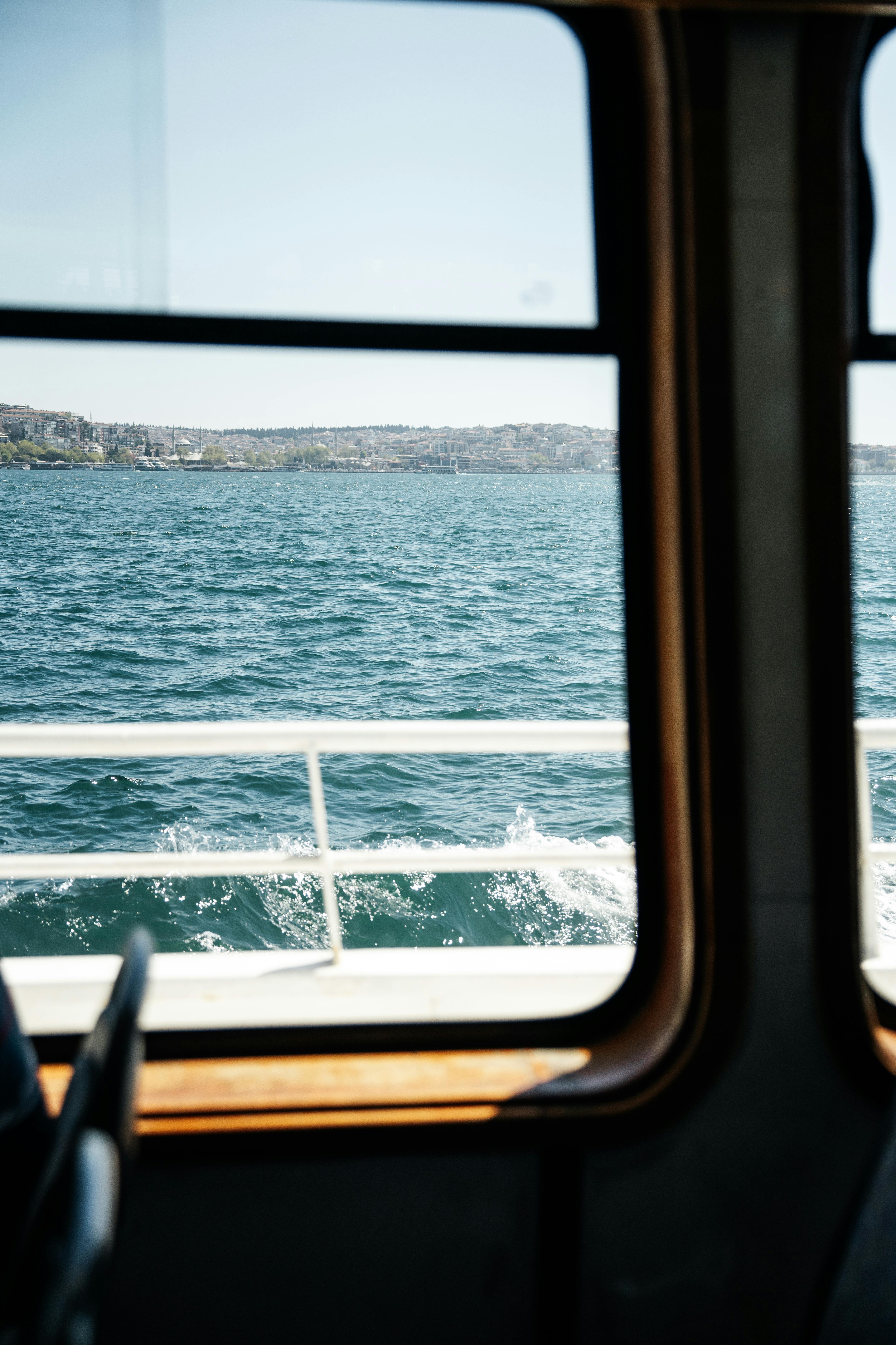 Peaceful ocean view through a ferry window with coastline in the distance. A serene travel moment captured on camera.